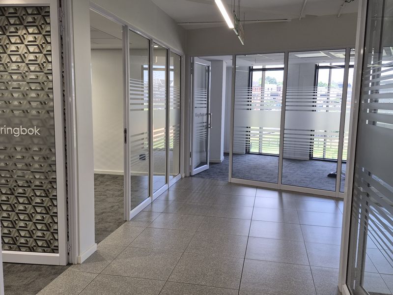 Modern office space featuring glass partition walls with frosted privacy film, tiled and carpeted flooring, and contemporary linear lighting.