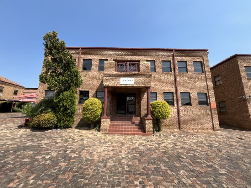 Front elevation of a face brick office building featuring a paved driveway, covered entrance with columns, and tiled steps.