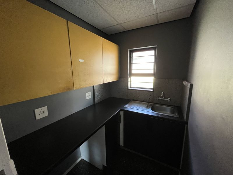A compact office kitchenette featuring built-in cabinetry, a dark laminate countertop, and a stainless steel sink with a window providing natural light.