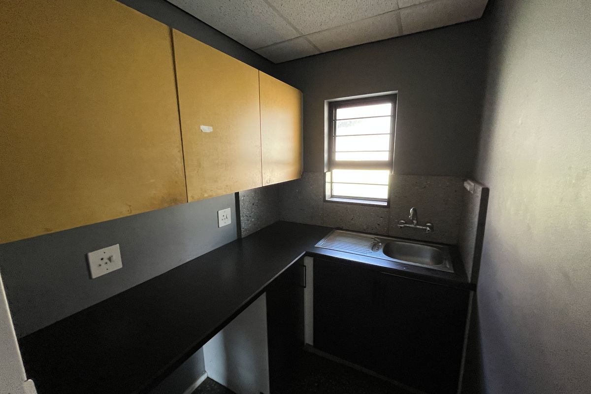 A compact office kitchenette featuring built-in cabinetry, a dark laminate countertop, and a stainless steel sink with a window providing natural light.