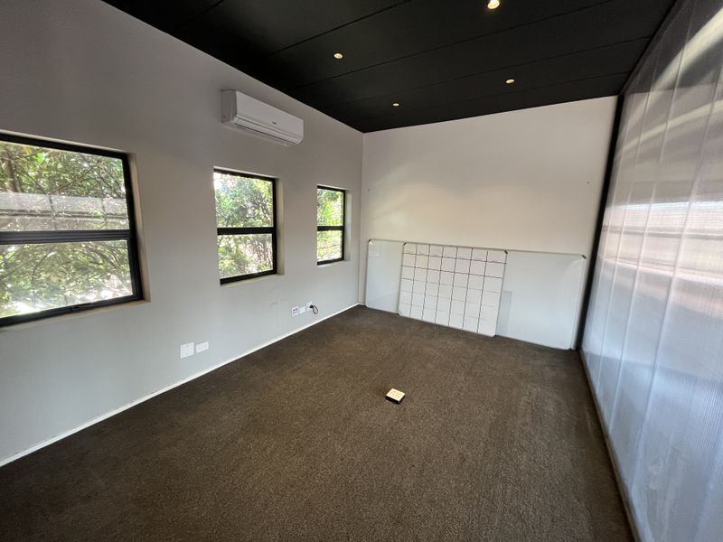 A clean, empty office space featuring dark carpeting, a contrasting black ceiling with recessed lighting, air conditioning, and a wall-mounted whiteboard.