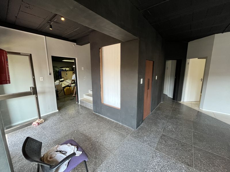 A spacious office hallway featuring dark painted ceilings, terrazzo flooring, and multiple access points to surrounding office rooms.