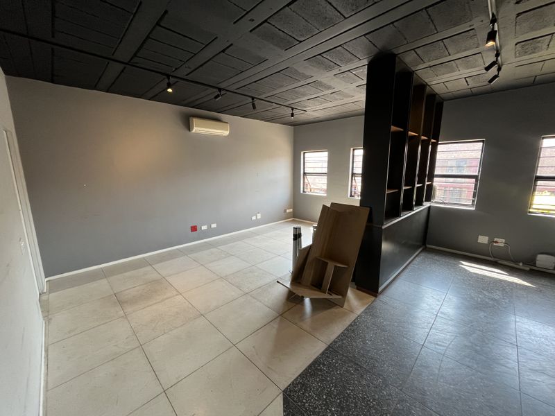 A modern, open-plan office space featuring tiled flooring, a built-in shelving partition, track lighting, and a split-system air conditioning unit.