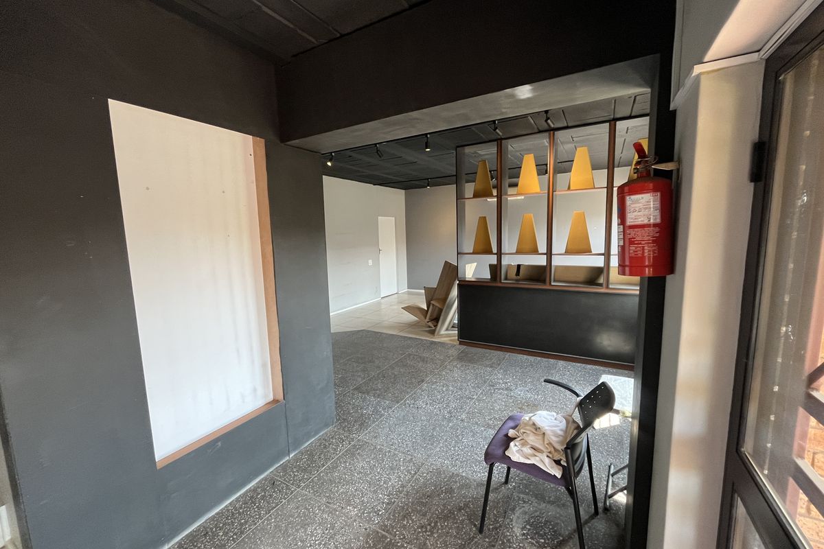 An open-plan office space featuring dark painted walls, terrazzo flooring, recessed ceiling lighting, and a built-in partition shelf unit.