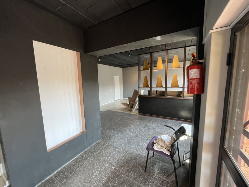 An open-plan office space featuring dark painted walls, terrazzo flooring, recessed ceiling lighting, and a built-in partition shelf unit.