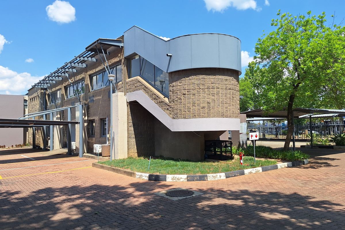 Exterior view of a commercial office building featuring a paved parking area, covered parking bays, and a prominent external staircase.