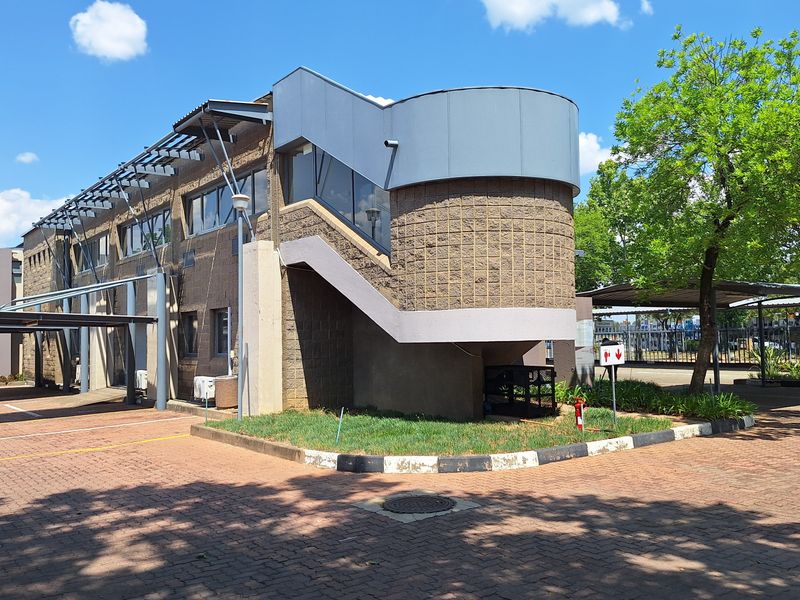 Exterior view of a commercial office building featuring a paved parking area, covered parking bays, and a prominent external staircase.