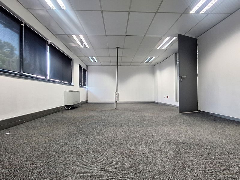 A spacious, empty office suite featuring a suspended ceiling, recessed lighting, carpeted flooring, and a central power pole for flexible workstation connectivity.