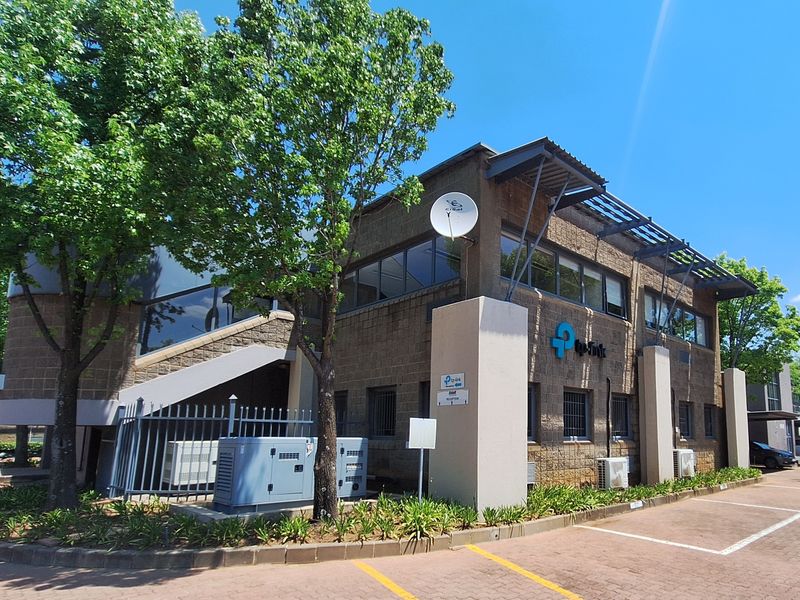 A well-maintained commercial office building featuring a brick facade, external staircase, and paved parking area with integrated security fencing and air conditioning units.