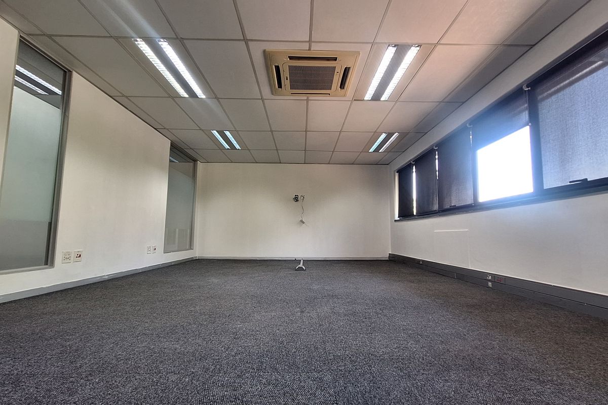 A spacious, empty office featuring a suspended ceiling with recessed lighting, integrated cassette air conditioning, carpeted flooring, and large windows with glass partitions.