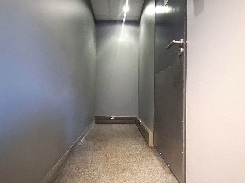 A narrow, empty office hallway featuring dark grey walls, carpeted flooring, and recessed ceiling lighting.