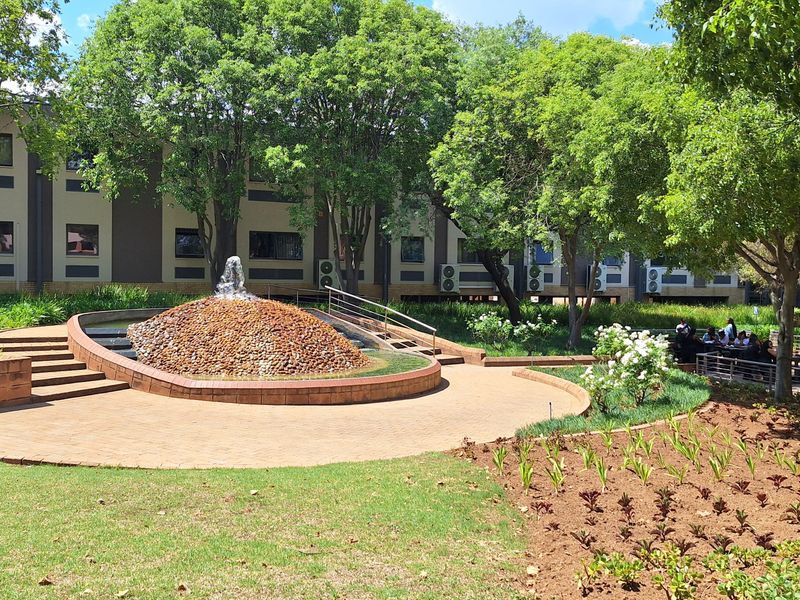 A well-maintained office park garden featuring a central water fountain, paved walkways, and mature trees, providing a pleasant outdoor space for occupants.