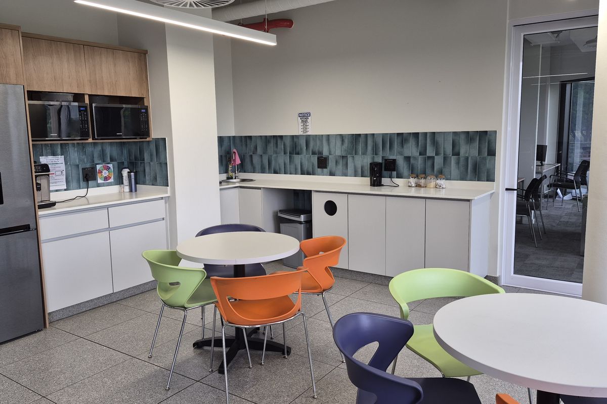A modern office kitchenette featuring clean white cabinetry, a stylish tiled backsplash, integrated microwave, and durable tiled flooring in a bright, functional workspace.
