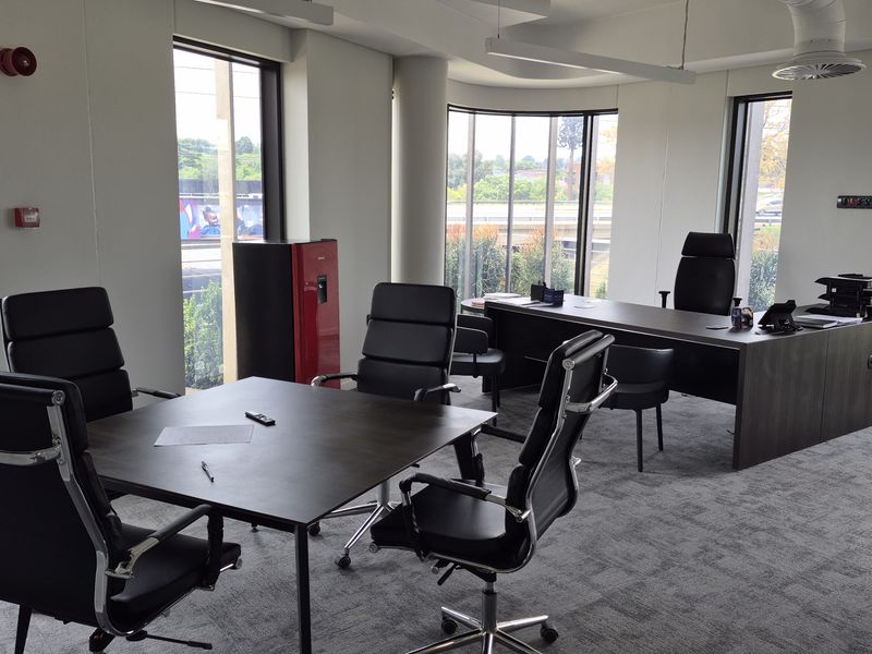 A professional office space featuring large floor-to-ceiling windows, carpeted flooring, and modern recessed lighting, providing a bright and functional workspace environment.