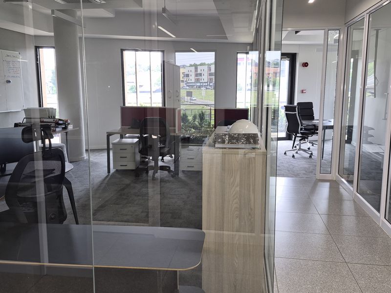 Modern office space featuring glass partition walls, a mix of tiled and carpeted flooring, and recessed ceiling lighting in a professional business environment.