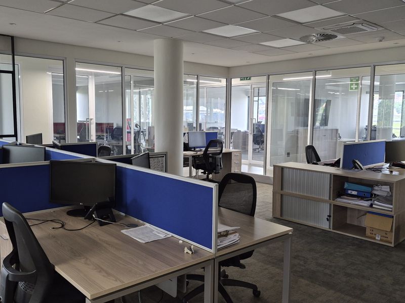 Modern open-plan office space featuring glass partitioning, suspended ceilings with recessed lighting, and carpeted flooring, providing a professional and bright work environment.