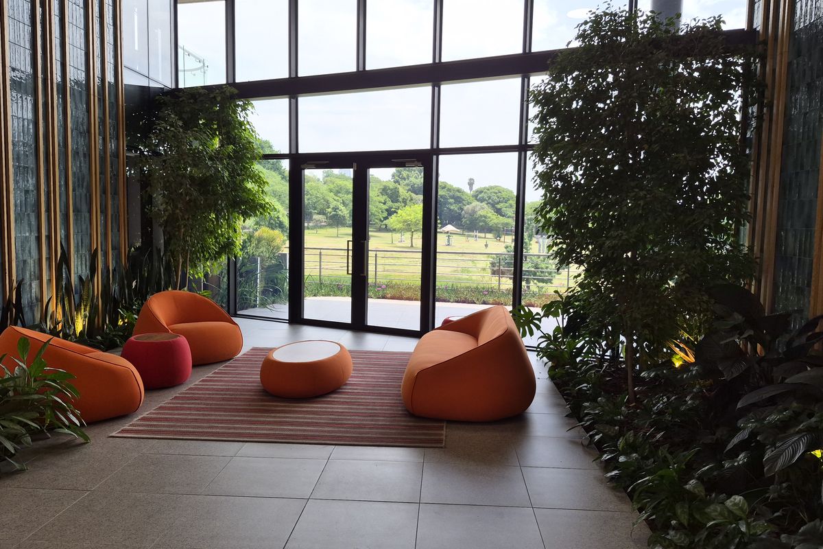 Modern lobby or lounge area featuring expansive floor-to-ceiling windows, tiled flooring, and integrated indoor greenery with views of the surrounding landscape.