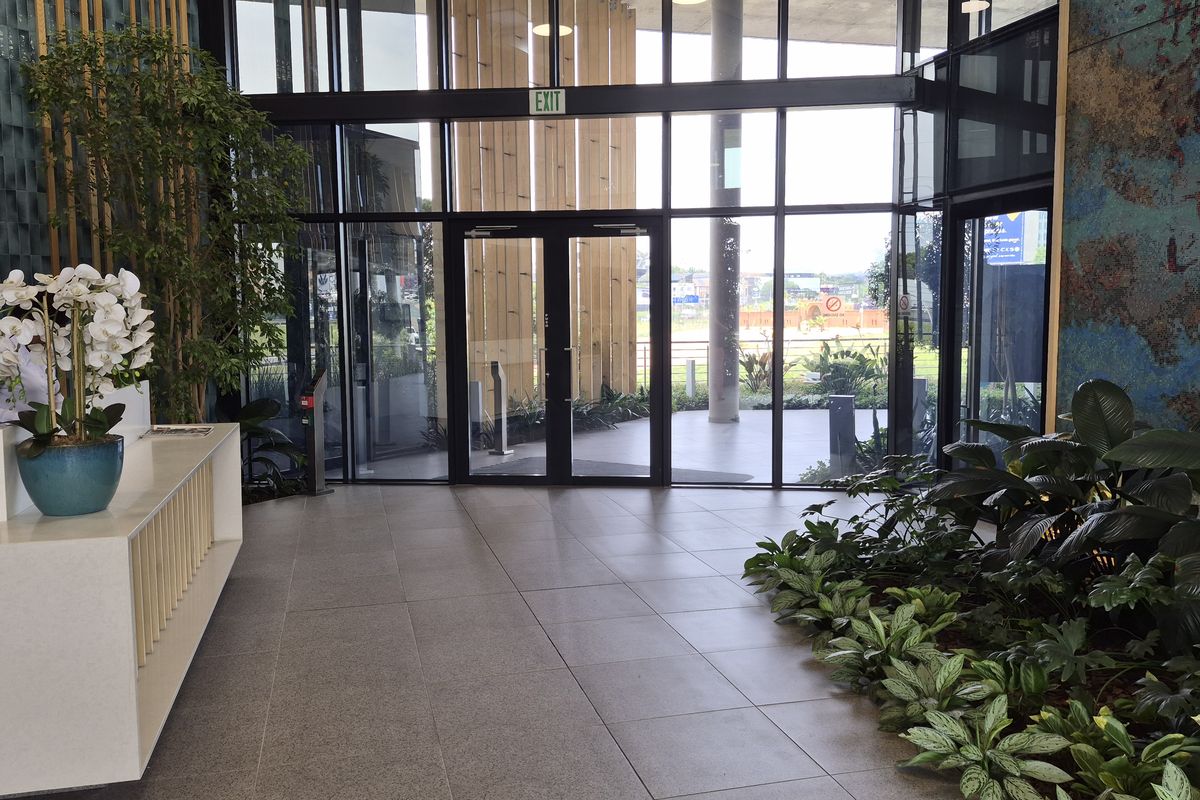 Modern commercial building entrance featuring floor-to-ceiling glass walls, double entry doors, tiled flooring, and a sleek built-in reception desk.