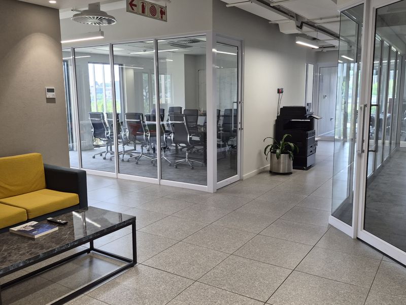 Modern office space featuring glass-partitioned meeting rooms, tiled flooring, and exposed ceiling services, creating a professional and bright corporate environment.