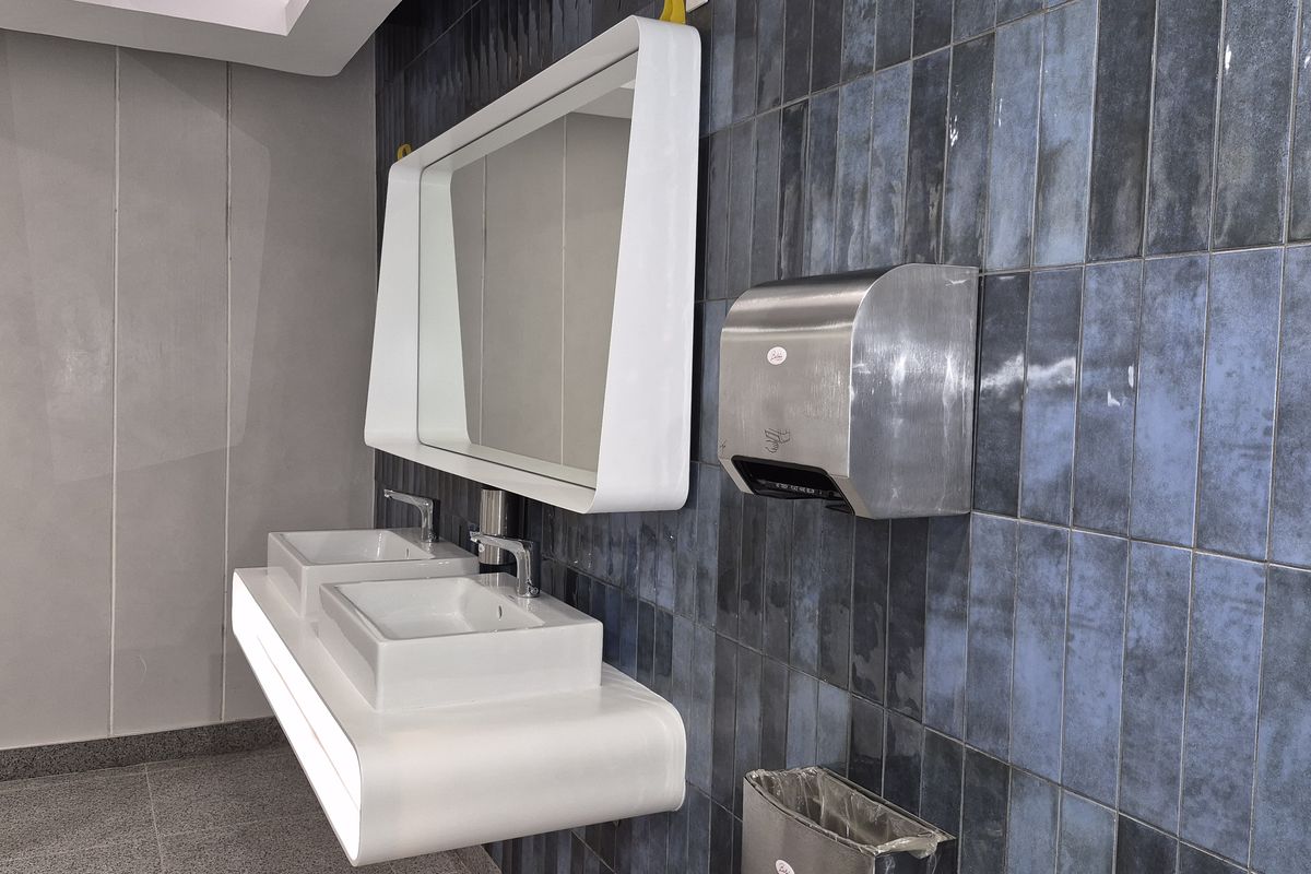 Modern commercial bathroom featuring a sleek double vanity with integrated mirror, wall-mounted basins, and stylish blue tiled feature wall with stainless steel hand dryer.