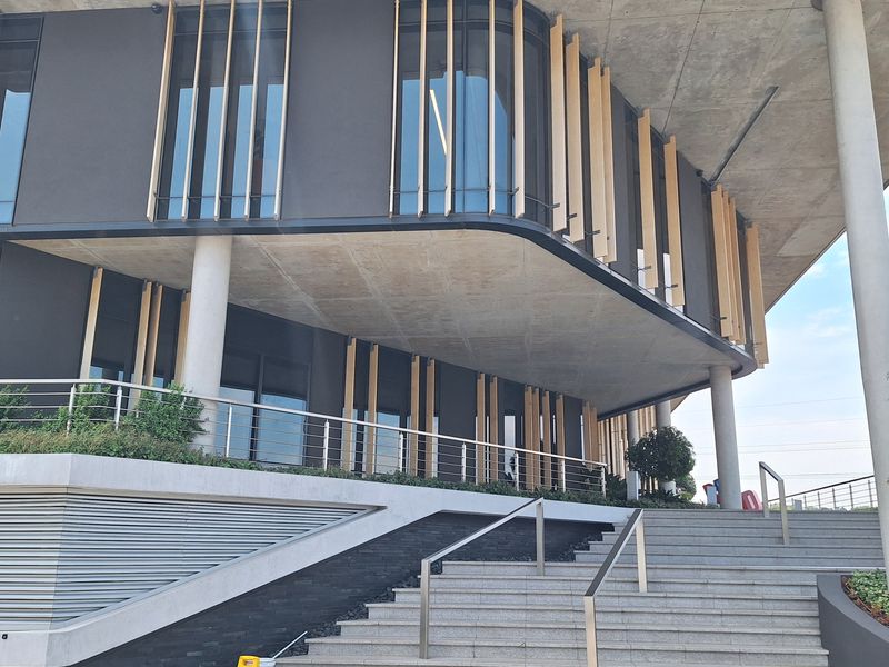Modern office building exterior featuring a striking concrete cantilevered roof, vertical timber louvers, and a grand stone staircase entrance.