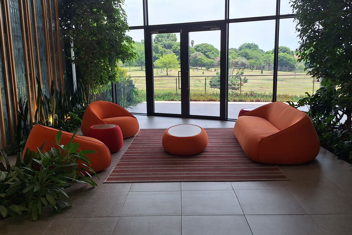 Modern office lounge area featuring floor-to-ceiling glass walls, tiled flooring, and elegant timber wall paneling with views of the surrounding landscape.