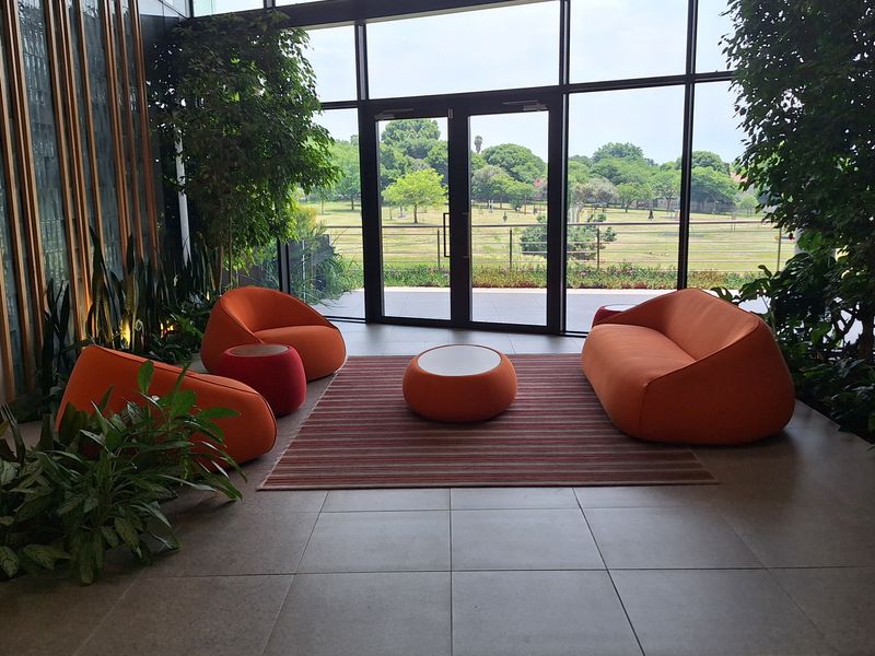 Modern office lounge area featuring floor-to-ceiling glass walls, tiled flooring, and elegant timber wall paneling with views of the surrounding landscape.