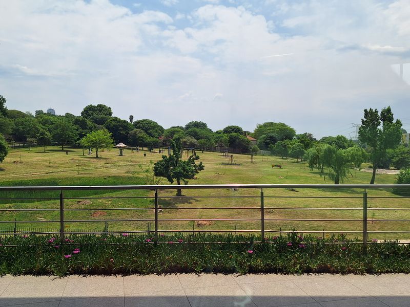 A clear view overlooking a landscaped park area, featuring a modern stainless steel balustrade and tiled flooring in the foreground.