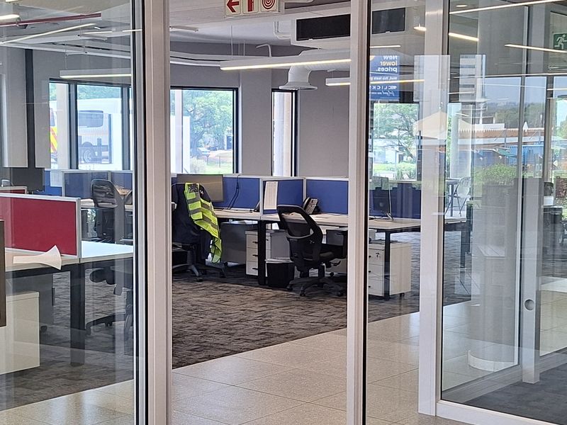 Modern open-plan office space featuring glass partitioning, suspended ceilings with linear lighting, and a mix of carpeted and tiled flooring.