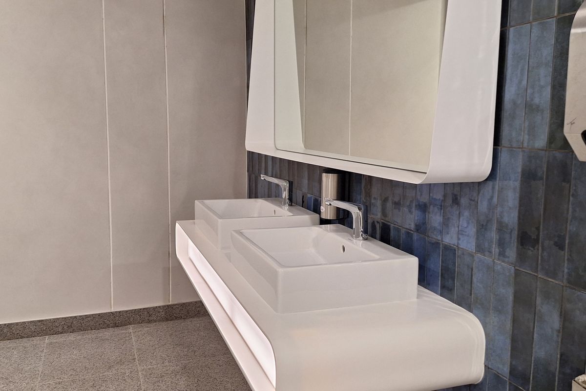 Modern office bathroom featuring a sleek, wall-mounted double vanity with integrated basins, chrome fixtures, and stylish blue tiled accent wall.
