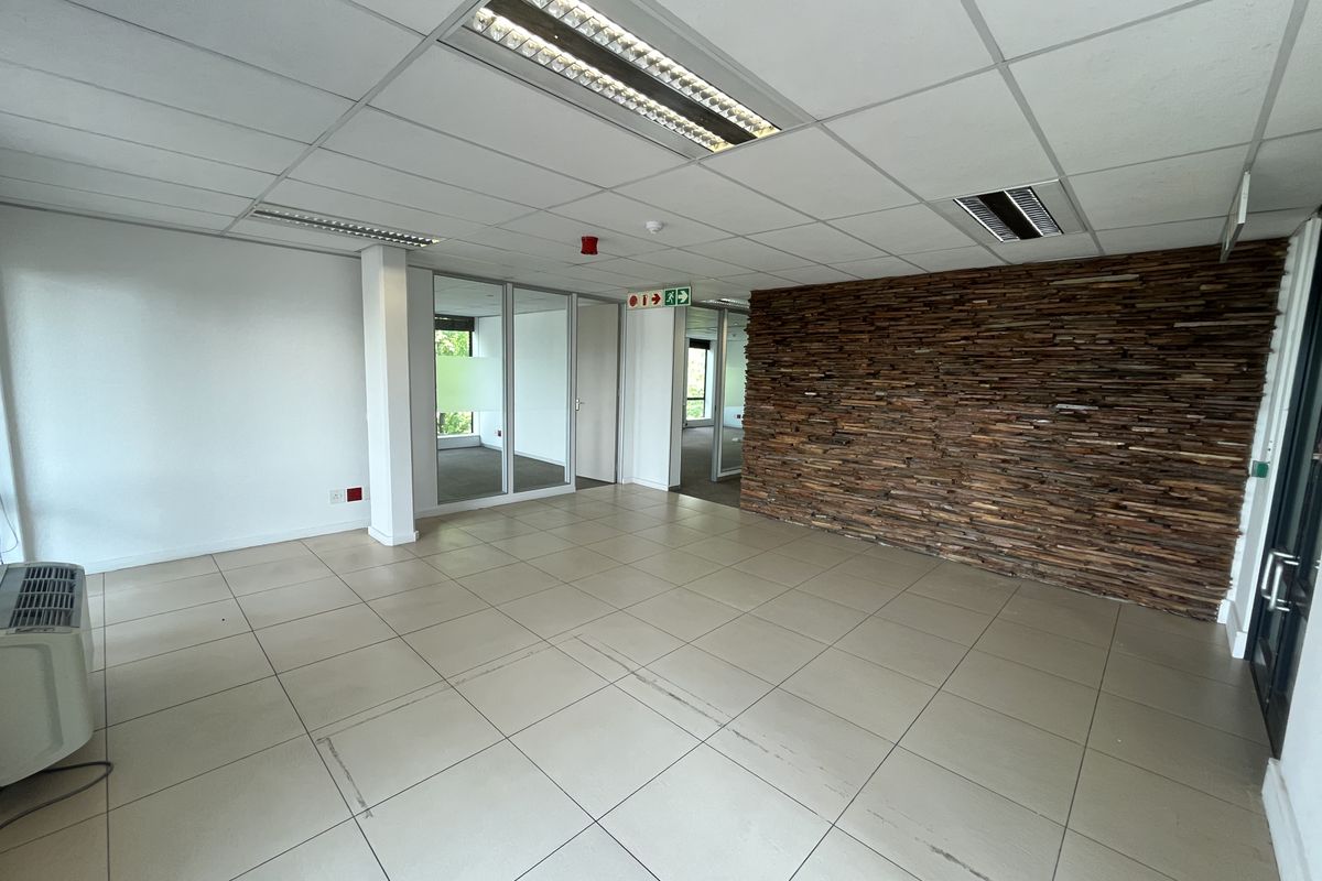 An open-plan office space featuring tiled flooring, a decorative stone feature wall, glass partitions, and recessed lighting in a suspended ceiling.
