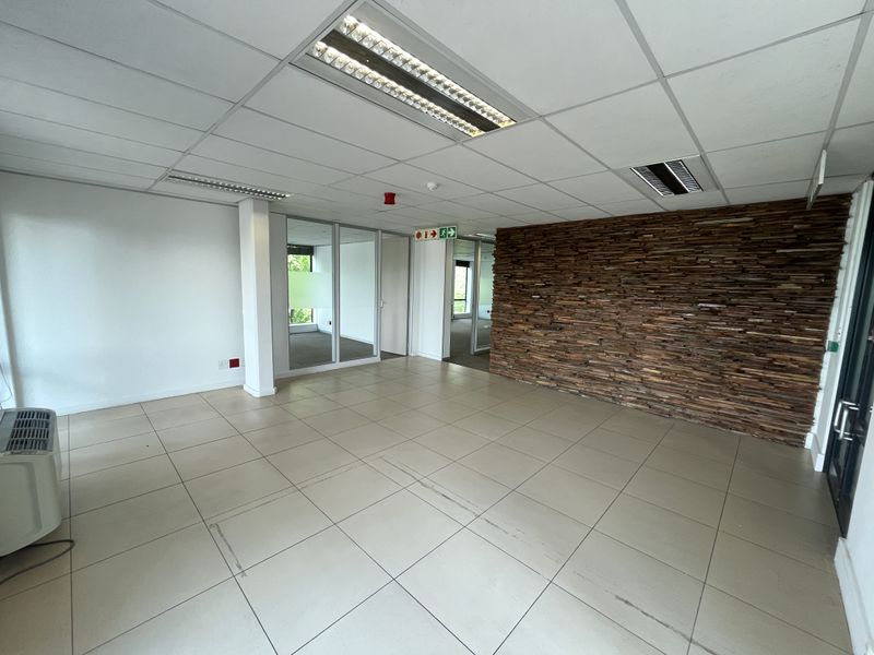 An open-plan office space featuring tiled flooring, a decorative stone feature wall, glass partitions, and recessed lighting in a suspended ceiling.