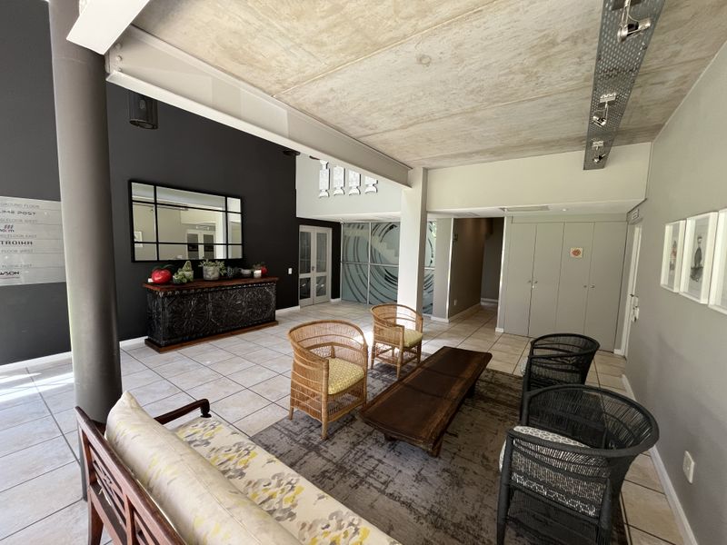 A modern office reception or waiting area featuring an exposed concrete ceiling, track lighting, tiled floors, and built-in storage cabinetry.