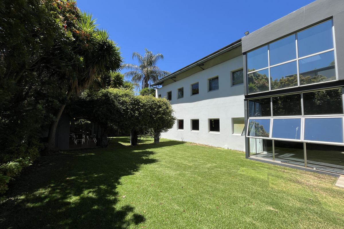 Rear view of the office building featuring a modern glass facade, large windows, and a well-maintained garden area with mature trees.