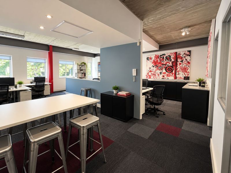 Modern open-plan office space featuring exposed concrete ceilings, recessed lighting, carpeted flooring, and integrated storage solutions in a professional, contemporary work environment.