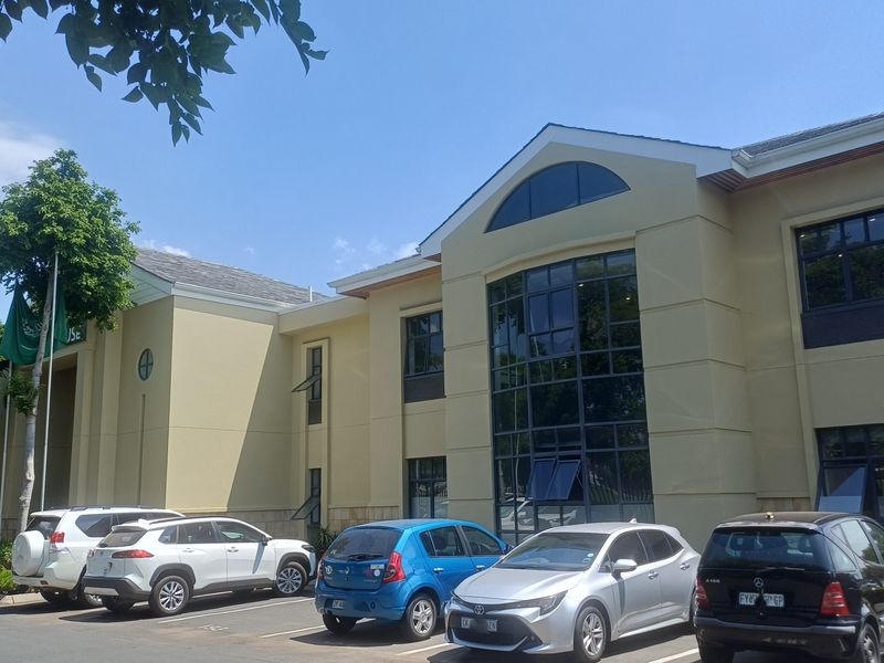 Front exterior view of a multi-story commercial office building featuring a prominent glass facade, arched window detailing, and an adjacent paved parking area.