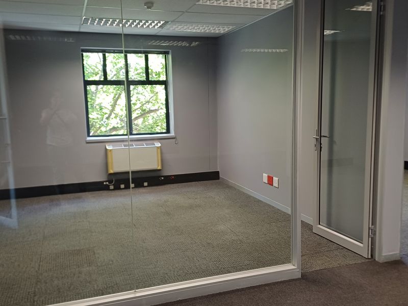 A vacant, professional office space featuring glass partitioning, carpeted flooring, suspended ceilings with recessed lighting, and an integrated HVAC unit.