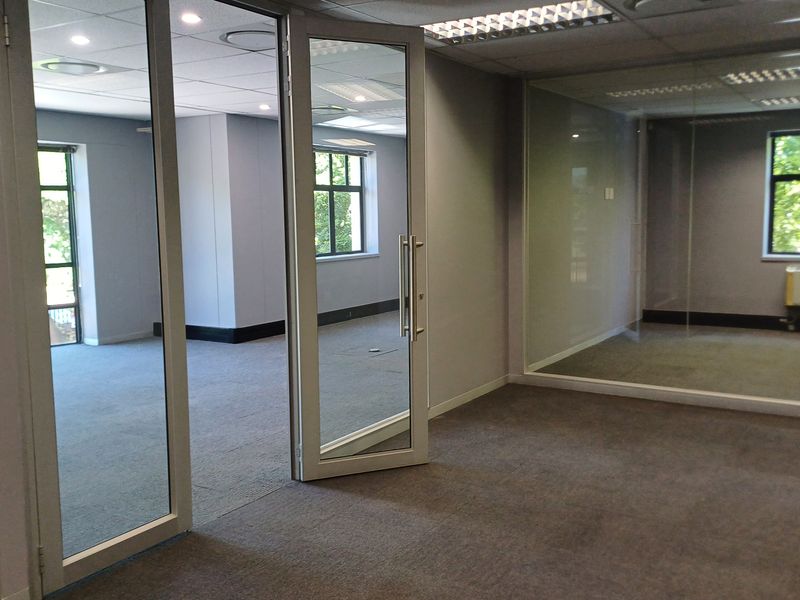 Modern vacant office space featuring glass partitioning, suspended ceilings, recessed lighting, and carpeted flooring, offering a professional and flexible work environment.