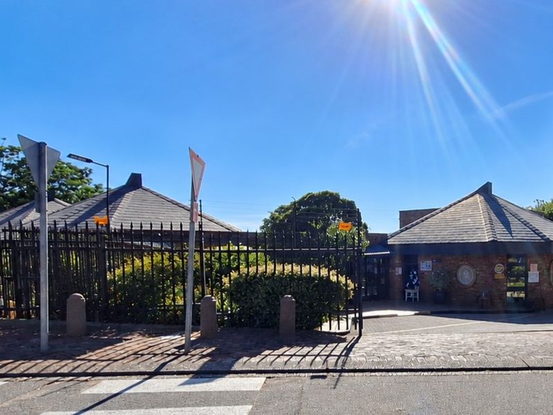 Front exterior view of a commercial property featuring a brick facade, hipped roof design, and secure gated entrance with paved driveway access.