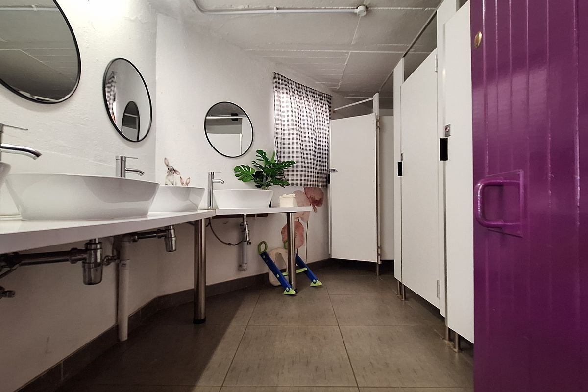 Commercial bathroom featuring multiple vessel sinks with chrome faucets, tiled flooring, and private toilet cubicles.