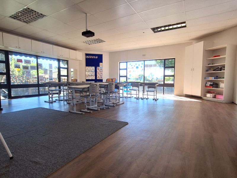 A bright and spacious classroom or office area featuring laminate flooring, built-in storage cabinetry, and large windows providing ample natural light.