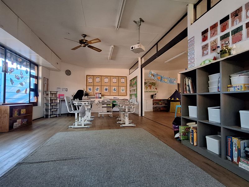 Spacious open-plan commercial area featuring laminate flooring, large windows for natural light, a ceiling fan, and integrated shelving, suitable for educational or office use.