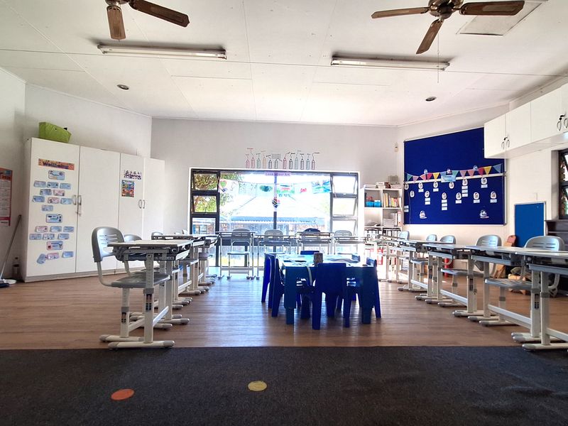 A spacious commercial classroom or office area featuring laminate flooring, built-in storage cabinetry, ceiling fans, and large windows providing natural light.