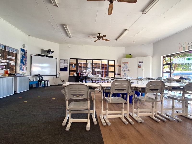 A spacious commercial office or classroom area featuring large windows, built-in storage cabinetry, ceiling fans, and integrated lighting fixtures.