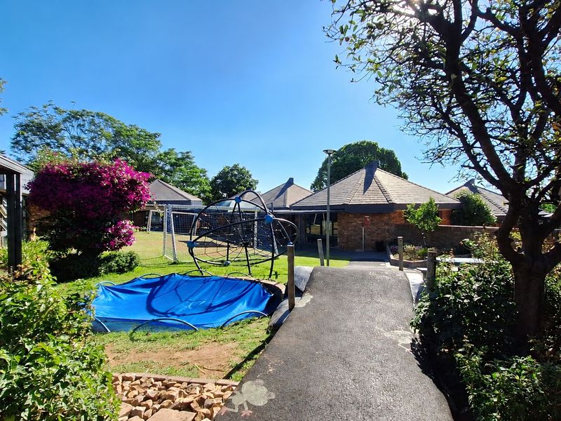 A well-maintained commercial garden area featuring paved pathways, established trees, and brick boundary walls, providing a pleasant outdoor space for the property.