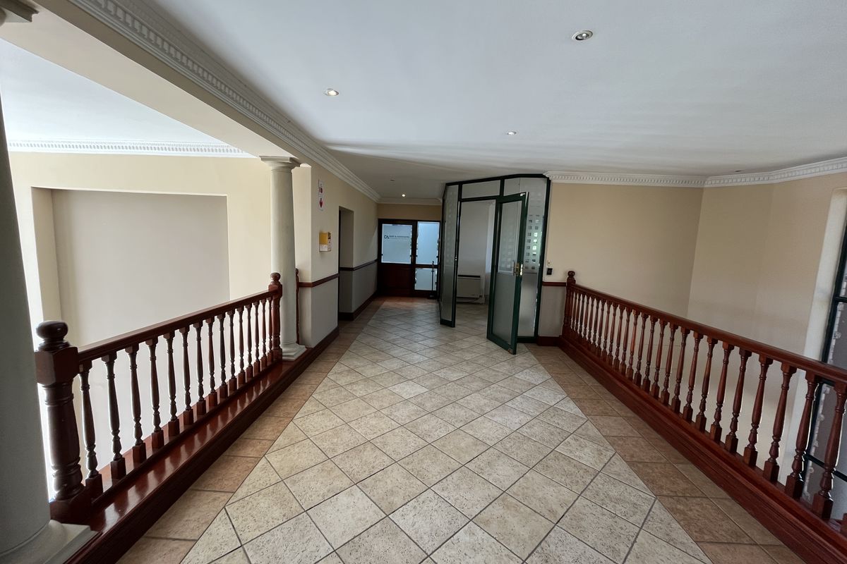 Spacious office hallway featuring tiled flooring, decorative ceiling cornices, recessed lighting, and a classic wooden balustrade overlooking the lower level.