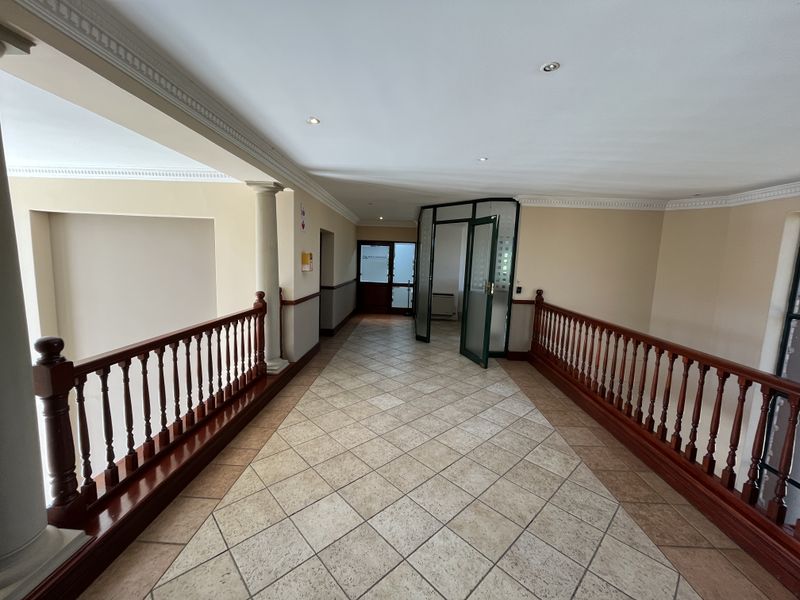 Spacious office hallway featuring tiled flooring, decorative ceiling cornices, recessed lighting, and a classic wooden balustrade overlooking the lower level.