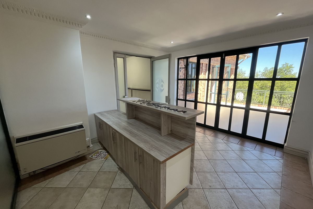 A bright office space featuring a built-in reception desk, tiled flooring, crown molding, and large black-framed glass doors leading to an outdoor area.