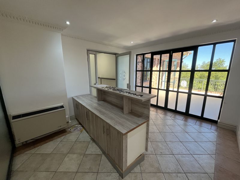 A bright office space featuring a built-in reception desk, tiled flooring, crown molding, and large black-framed glass doors leading to an outdoor area.
