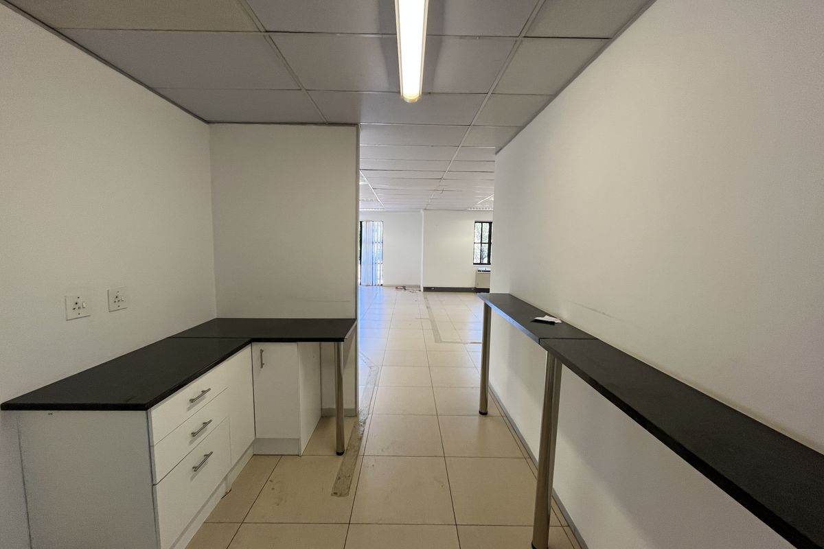 An empty office space featuring tiled flooring, a suspended ceiling, built-in cabinetry with a dark countertop, and a long wall-mounted desk surface.